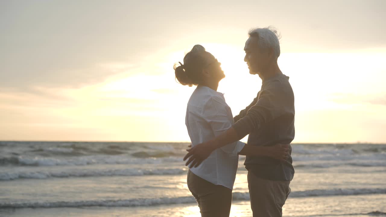 아시아의 한 부부가 해가 지면 해변에서 서로 포옹하고 있습니다.