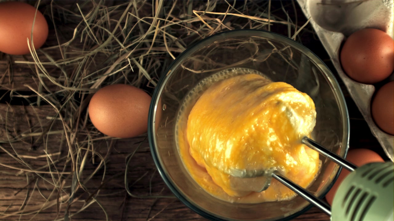Electric Mixer Beating Raw Eggs in a Glass Bowl