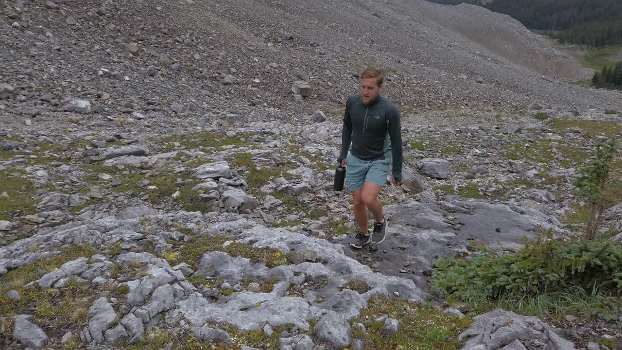 Nærbilde av vandrer på vei opp et fjell, med innsjø og skog som omkranser Rocky Mountains i Kananaskis, Alberta, Canada.