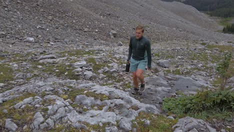 Hiker-walking-up-mountain-with-lake-and-forest-circling-close-up-Rockies-Kananaskis-Alberta-Canada