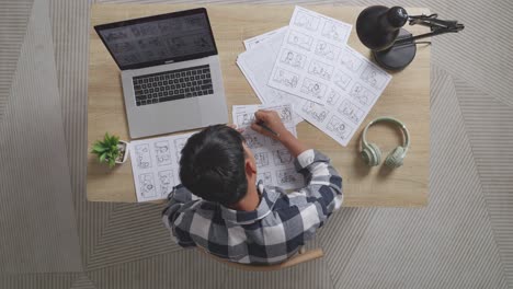 top view of asian male artist celebrating succeed while drawing storyboard for the film on the table with a laptop and headphones in the studio