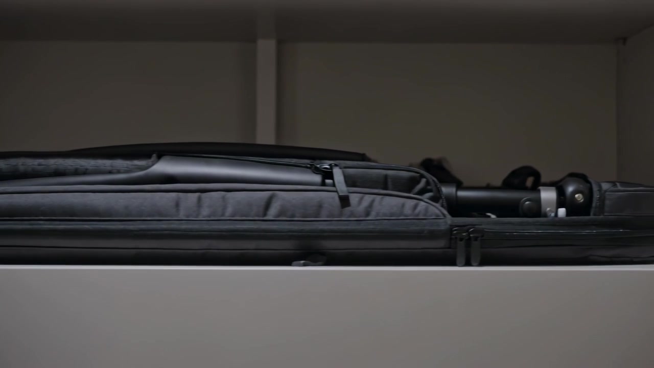 Camera shifting revealing stacked gray black equipment cases on white shelf, tripod emerging
