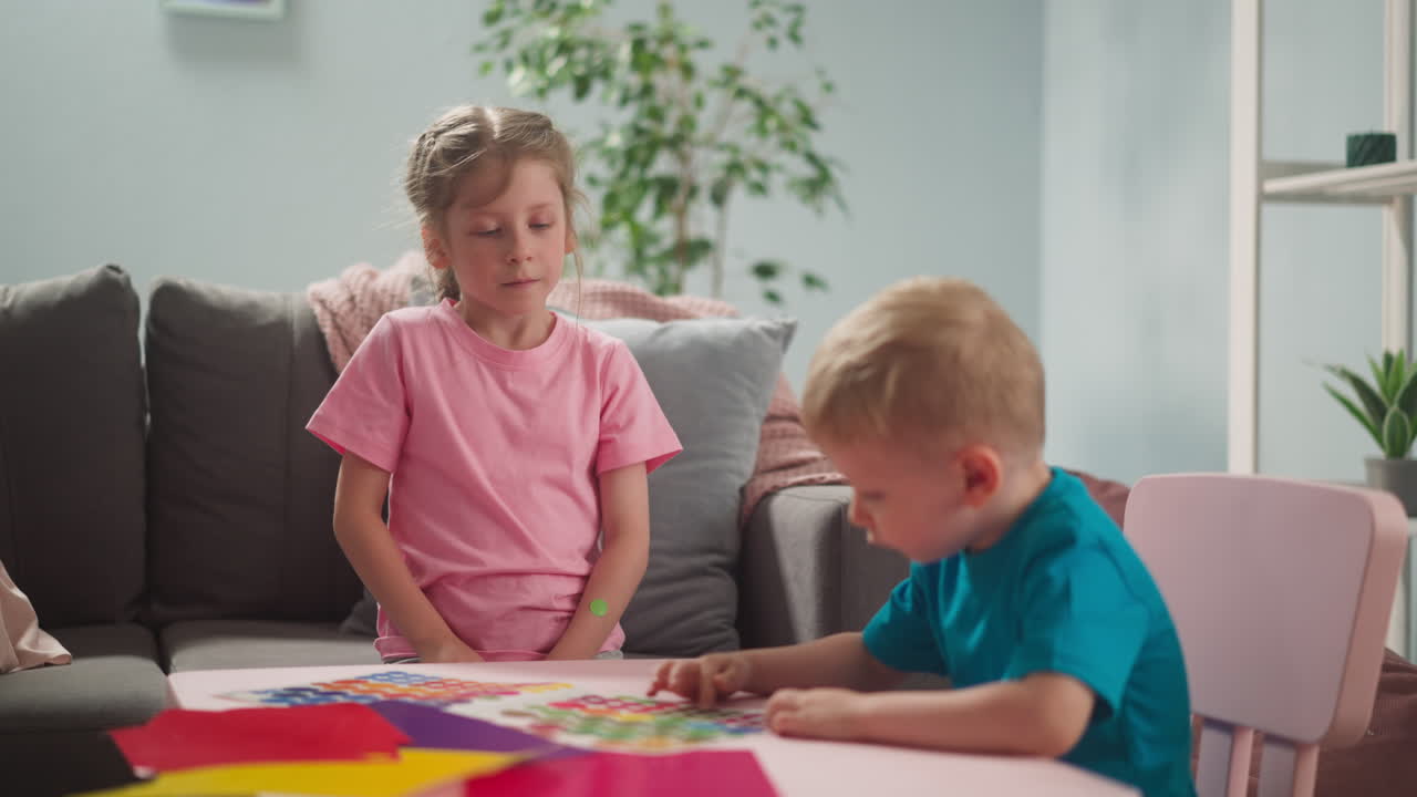Il bambino guarda un adesivo a pois colorato, la sorella è seduta vicino.
