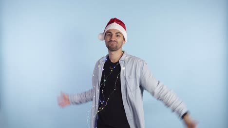 Crazy,-handsome-excited-man-throwing-dollar-banknotes-and-smiling.-Squandering,-wealth.-Man-in-a-santa-red-hat-and-garland-on-neck-standing-isolated-on-blue-background