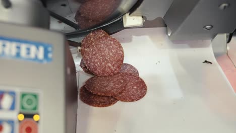 salami-scheiben, die von einer kommerziellen fleischschneidemaschine an einer feinkost-fleischtheke fallen