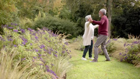 Senior-biracial-couple-dancing-together-in-sunny-garden,-unaltered,-copy-space,-in-slow-motion