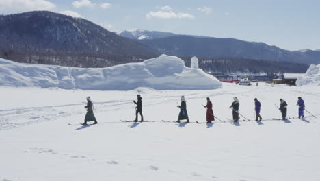 tuva men dressed in traditional robes walking in snow with fur skis on winter day, aerial epic