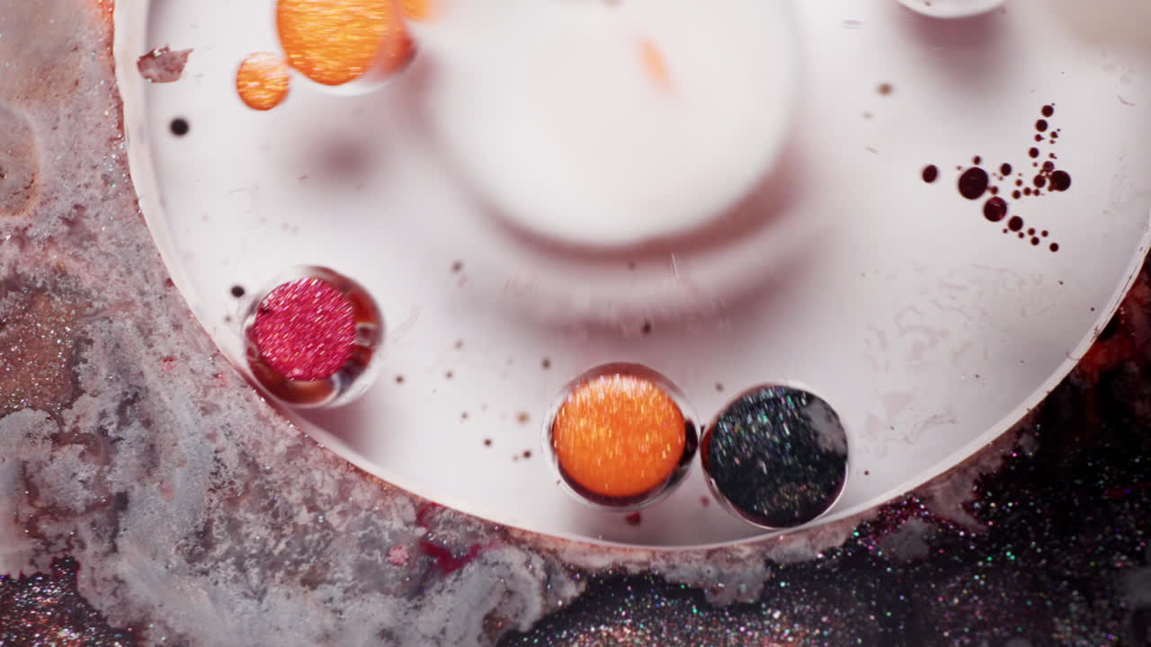 Macro slow-motion shot of an impact disturbing glittery red, orange, and brown ink bubbles, creating fluid blasts and mixing effects