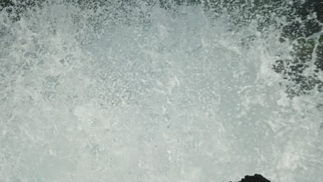 strong waves crash bursting up against black basalt lava rocks on coast in slow motion