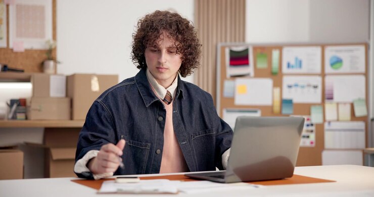 Joven trabajando en su portátil y tomando apuntes en la oficina
