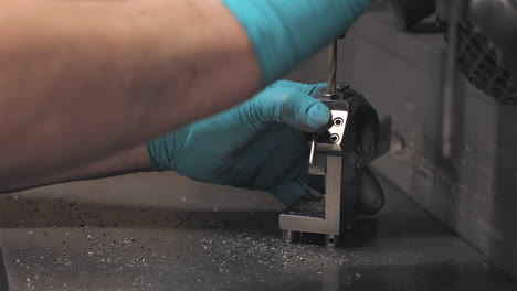 close-up of a technician using a drill press and fixture to machine a small metal part, showcasing precision craftsmanship in a manufacturing setting.
