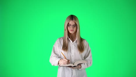 Joven-Mujer-Rubia-Escribiendo-Notas-En-Un-Cuaderno-De-Papel-Sobre-Fondo-Verde,-Fotografía-De-Estudio