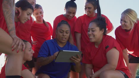 Female-Coach-Discussing-Tactics-With-Womens-Soccer-Team-Using-Digital-Tablet-Before-Match