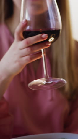 young woman with plate of fresh salad takes large wineglass and drinks wine sitting at table during festive dinner at home closeup slow motion