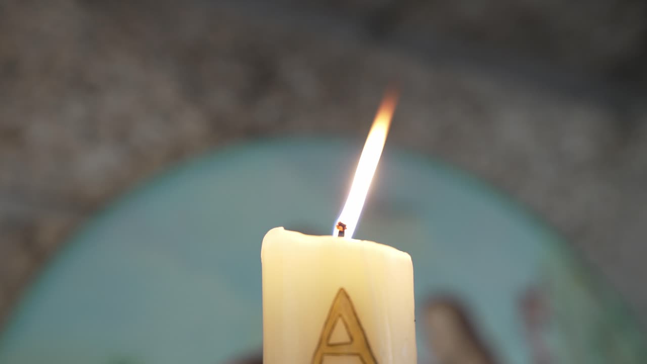 Close up of a lit candle with a carved alpha symbol and soft background blur