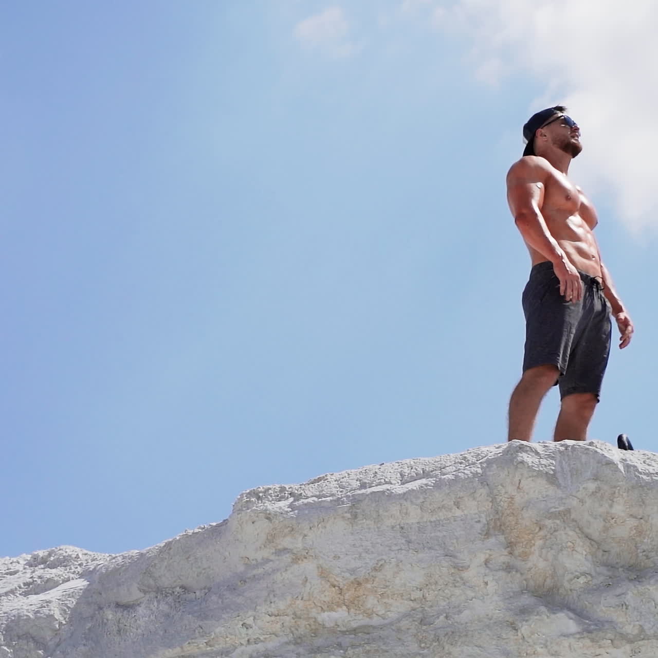 Shirtless athlete with strong body resting after heavy training on the sky background. Muscular man without shirt on white hill outdoors.