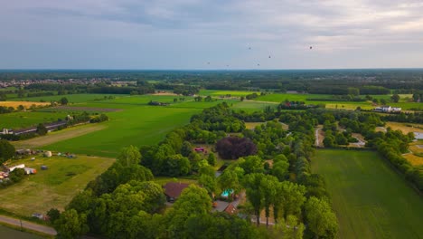 Hot-air-balloons-ascend-and-descend-over-flat-landscape-of-Europe,-aerial-hyper-lapse-view