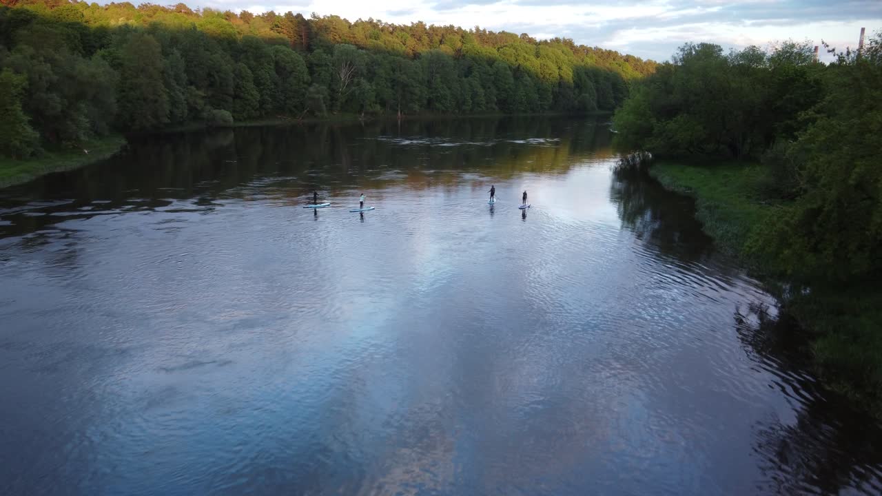 Gruppe mennesker paddleboarder på floden under solnedgang, luftfoto fra drone