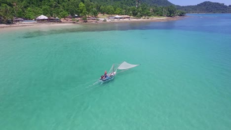 aerial dolly shot of a traditional shrimp fisherman on small wooden boat in thailand with beach and resorts in the background