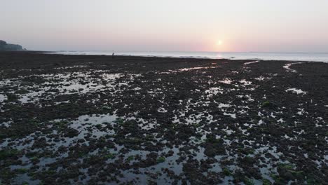 Disparo-De-Drones-En-ángulo-Bajo-Moviéndose-Sobre-El-Arrecife-De-Marea-Baja-De-La-Playa-De-Bingin-Con-Puesta-De-Sol-En-Uluwatu-Bali-Indonesia