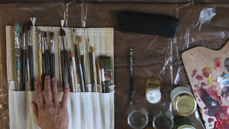 top-shot-of-a-painter-hesitating-between-a-bunch-of-brushes-on-his-workbench-and-finally-picking-one