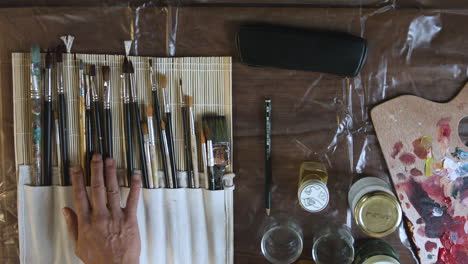 top shot of a painter hesitating between a bunch of brushes on his workbench and finally picking one