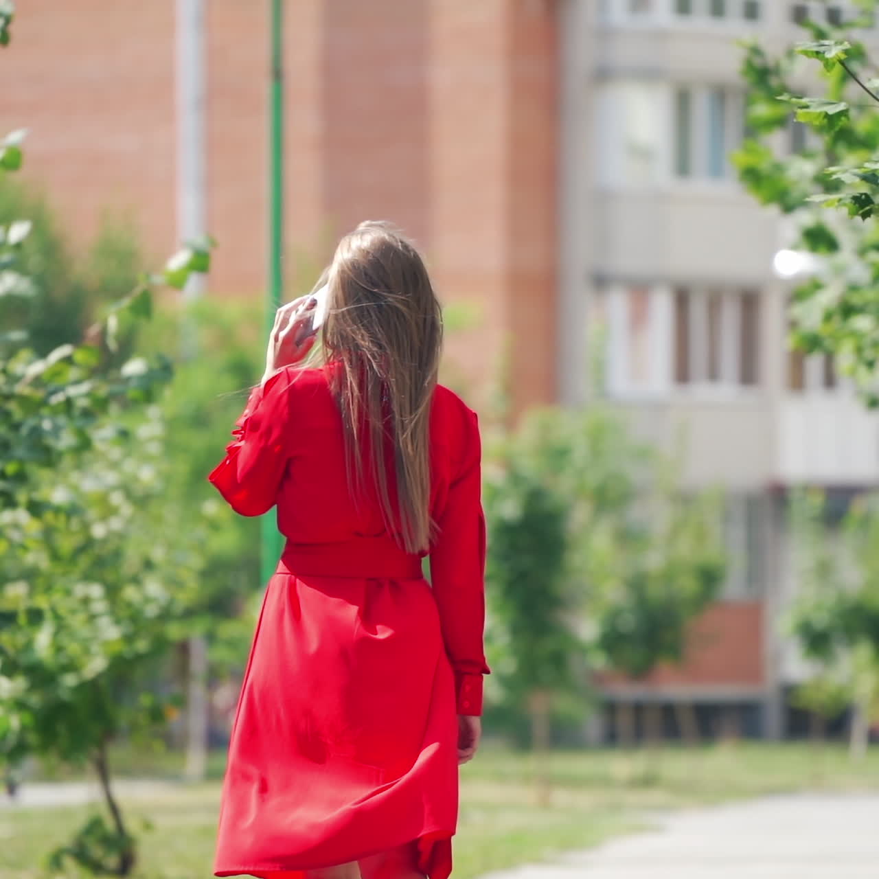 Gorgeous woman in red dress in the city. Young woman with long hair talking on the phone on the city background. Sllow motion.