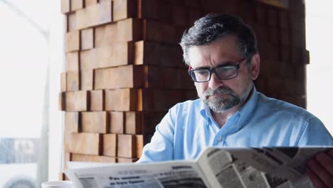senior man reads a newspaper sitting in a cozy cafe