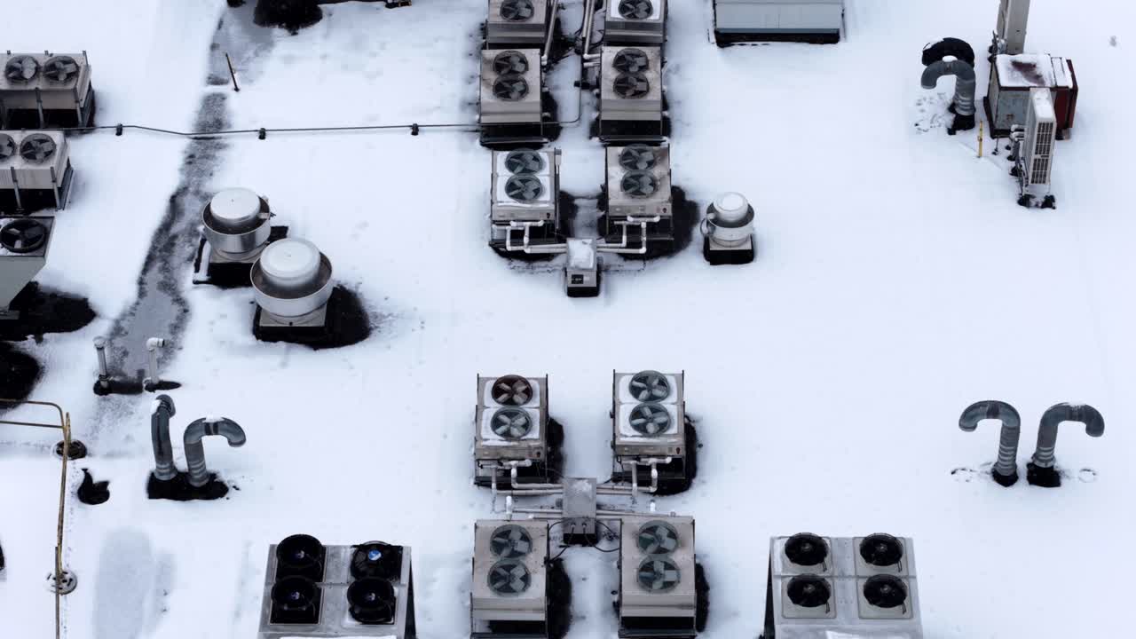 Commercial building roof covered in snow in the United States. Industrial ventilation systems and HVAC units during winter. Aerial top down shot