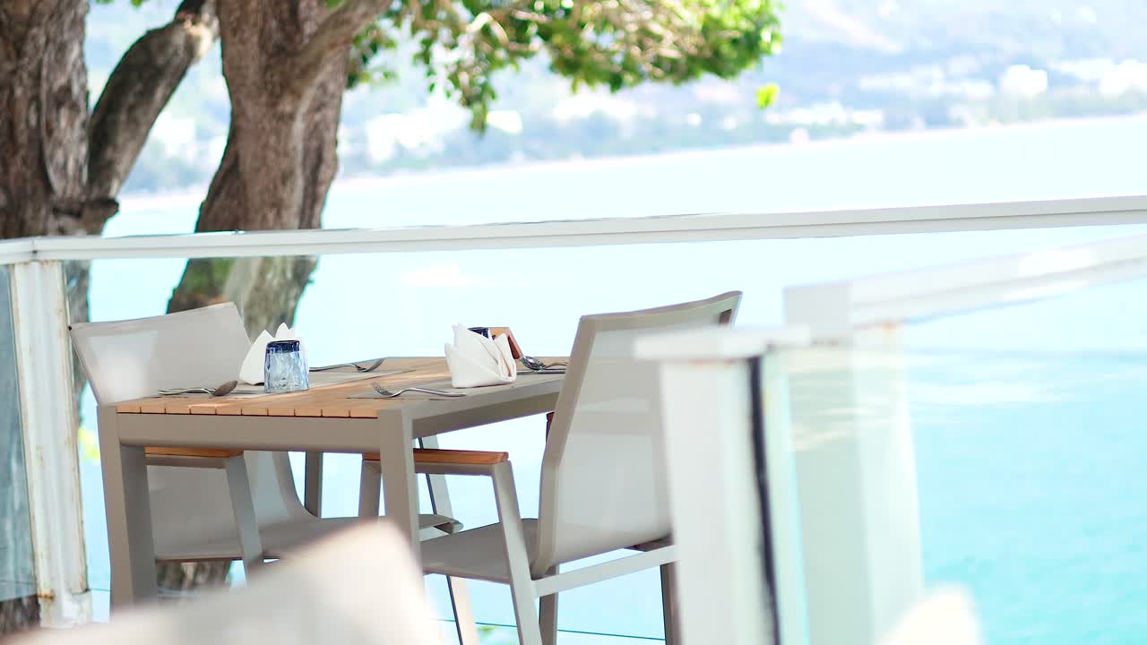 Outdoor dining setup overlooking the ocean in Phuket. Bright daylight, tranquil atmosphere, with a focus on natural beauty and relaxation