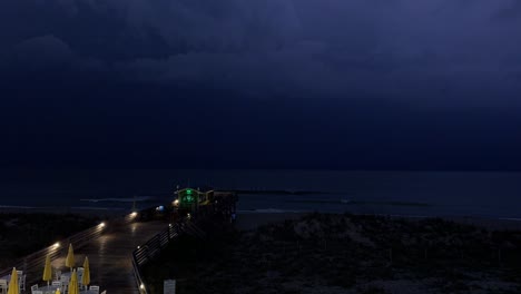 thunder and lightning during a spring storm on the beach with a pier in the foreground