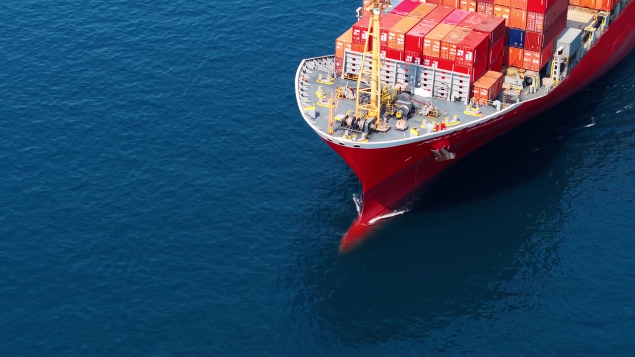 Proa de buque portacontenedores navegando por un mar azul en calma, vista aérea que muestra el transporte marítimo