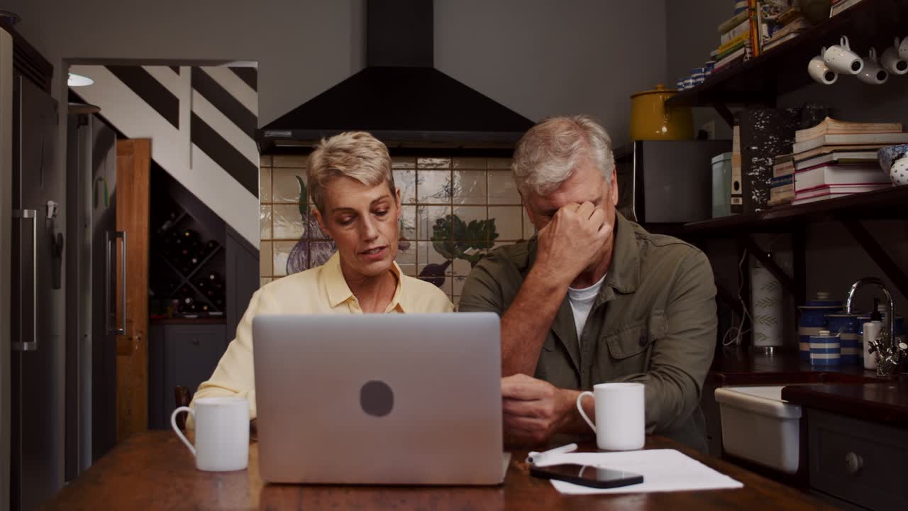 una linda pareja de ancianos sentada en la cocina clasificando documentos