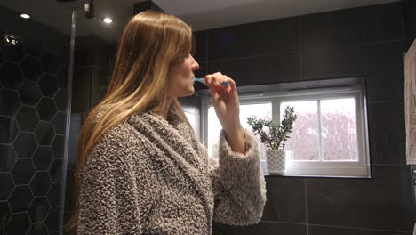 female model brushing teeth in a modern bathroom with a bathrobe, dressing gown on