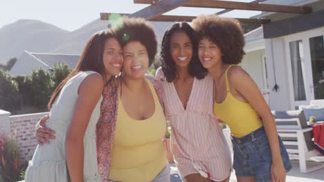 Portrait-of-happy-diverse-female-friends-embracing-and-smiling-at-swimming-pool-party