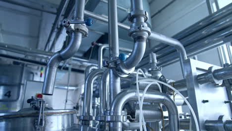 bended pipes with sluices and faucets. stainless steel pipe constructions at the dairy manufacturing plant. silver pipes shining at the light from a window.