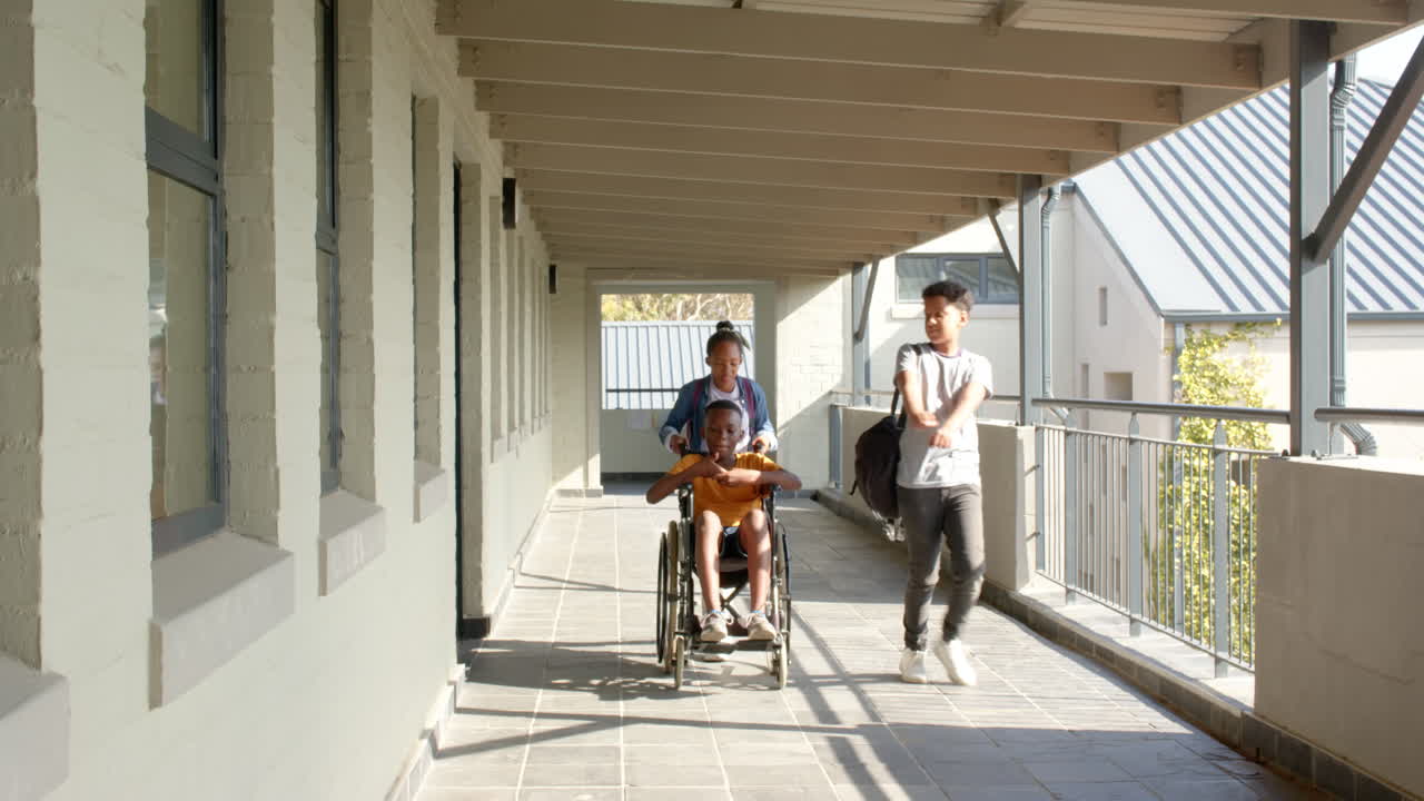 Walking in school hallway, multiracial students, one pushing friend in wheelchair, copy space