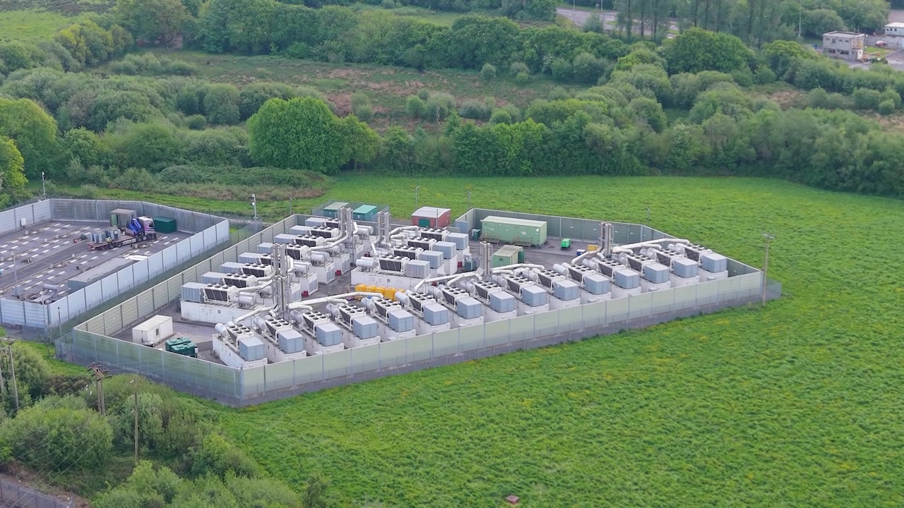 Pushing Aerial Towards Modern Gas Peaking Plant with exhaust stacks, generators, cooling systems. Facility provides rapid-response electricity to the grid during peak demand. Energy in UK.