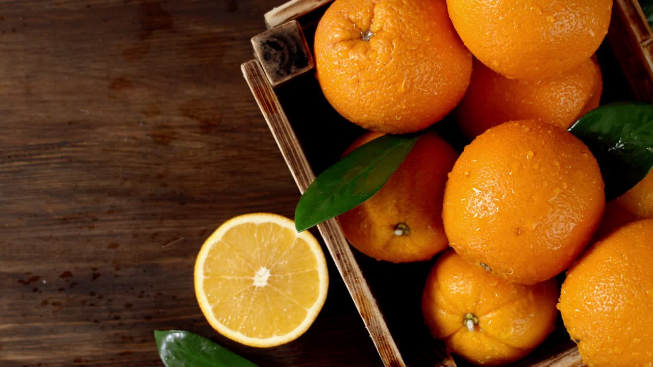 naranjas con hojas en una caja de madera cayendo gotas de agua.