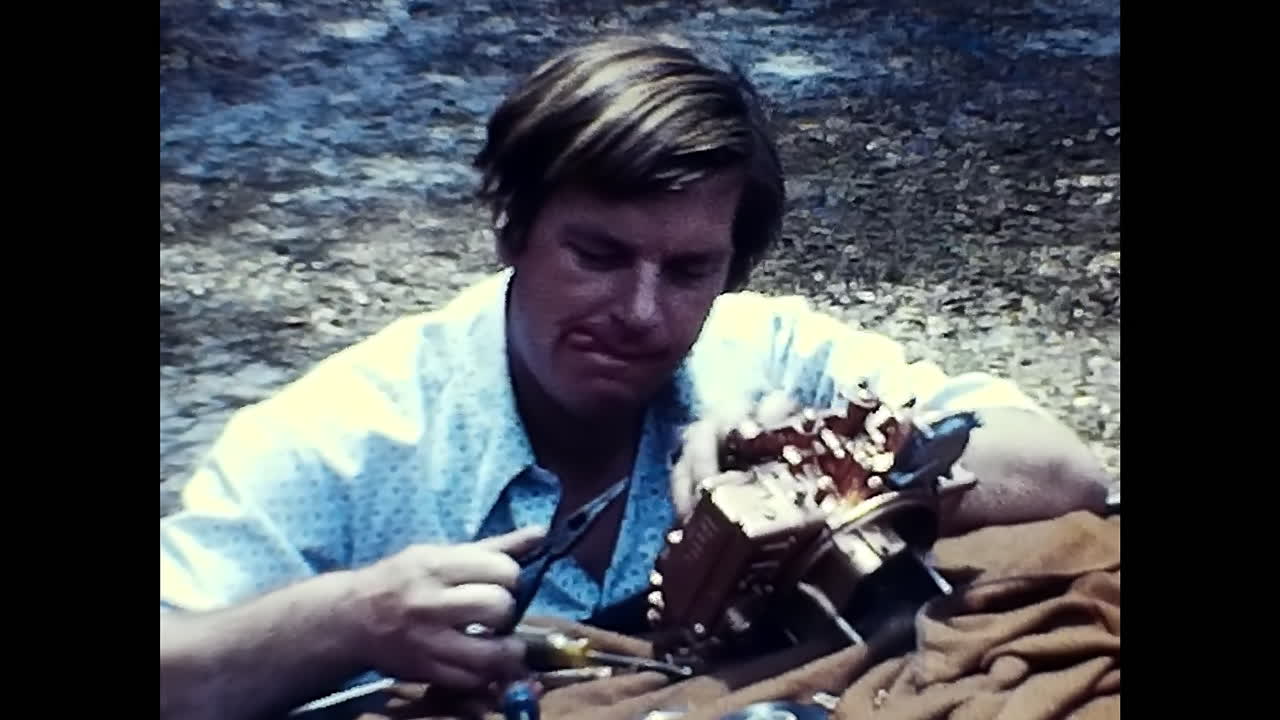 Man Sitting at Table, Focused on an Object at an Old Car Show in 1970s USA. CIRCA USA - 1970s: A man sitting at a table, completely engrossed in examining something at an old car show in 1970s USA.