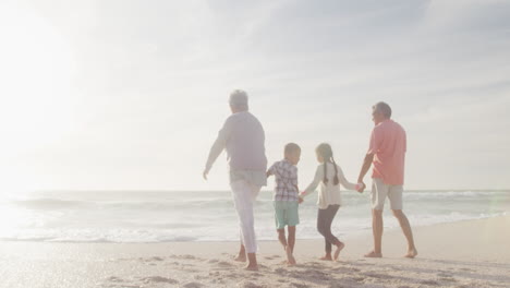 Glückliche-Hispanische-Großeltern-Und-Enkelkinder,-Die-Bei-Sonnenuntergang-Am-Strand-Spazieren-Gehen