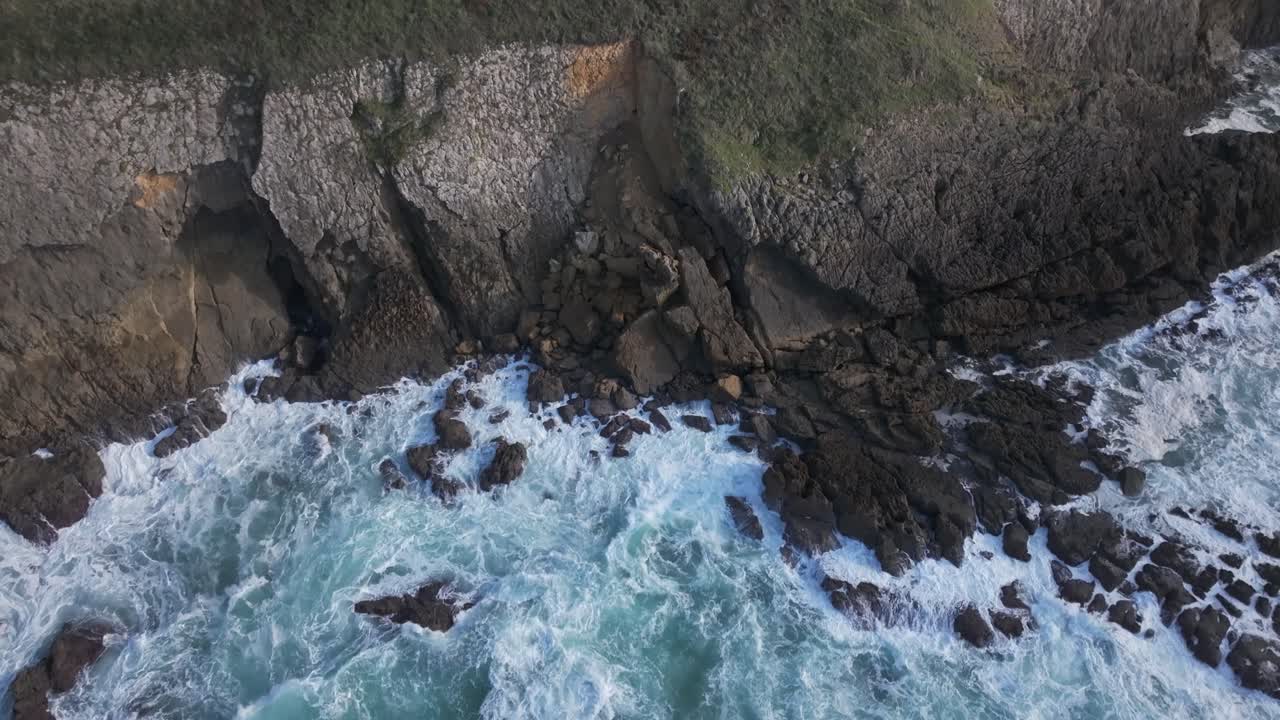 Drone flight from behind, starting over the rugged Cantabrian cliffs and moving smoothly towards the open sea. Waves crash below, forming white foam against the rocks