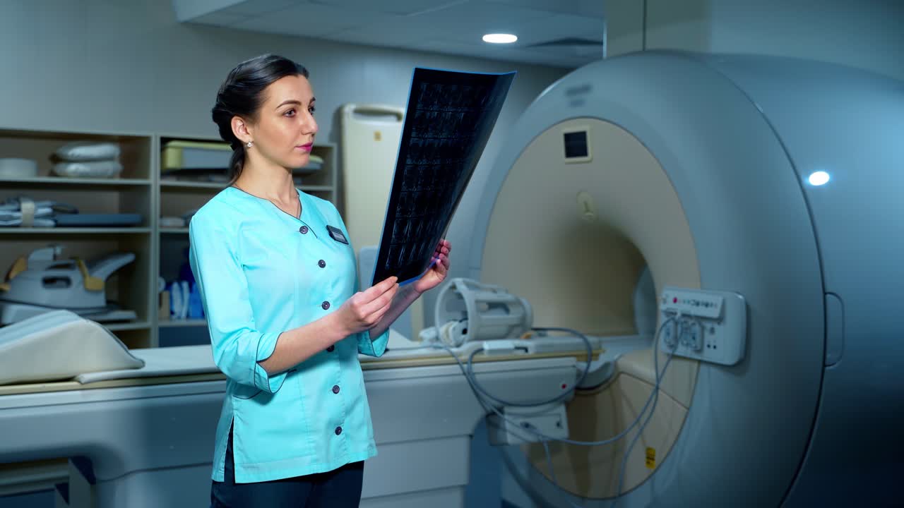 Female doctor examining x-ray photo. Beautiful medic standing in the modern clinic and looking at radiology scan. Advanced equipment in the hospital.