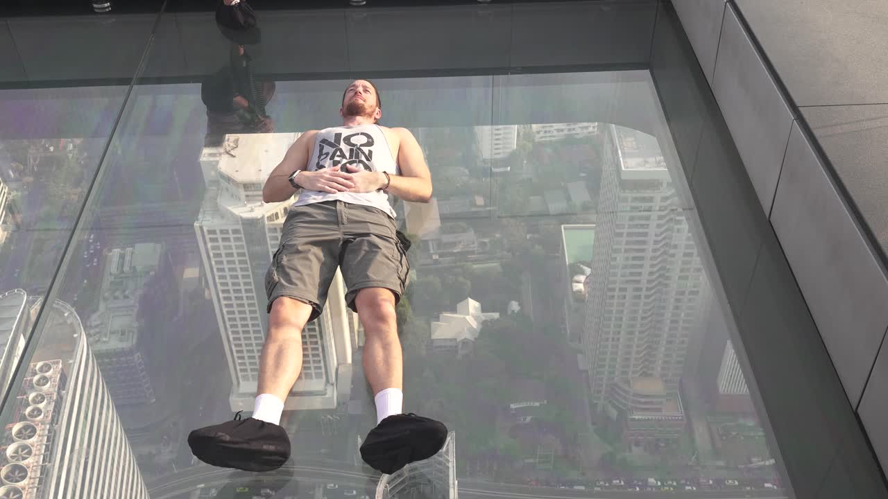 Hand-held shot of a tourist lying down on the glass floor at the Manahakhon skyscraper