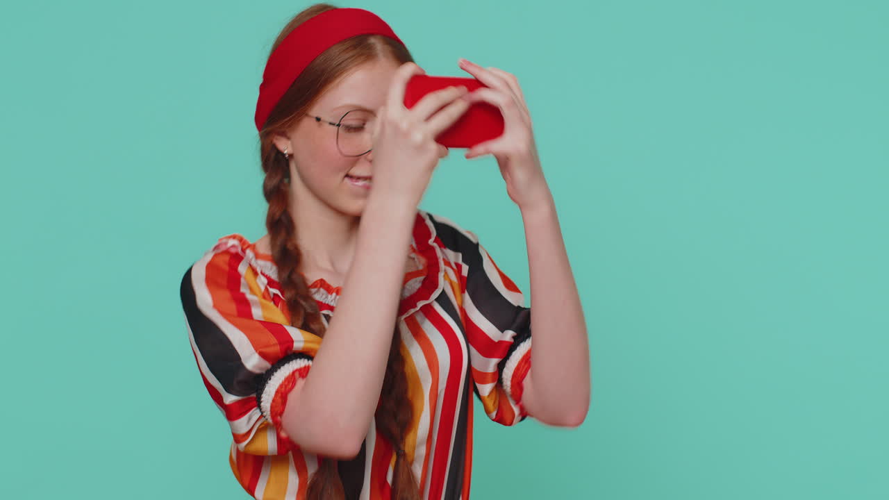 preocupada, graciosa, adicta, pelirroja, jugando con entusiasmo a un videojuego de carreras en su teléfono móvil.