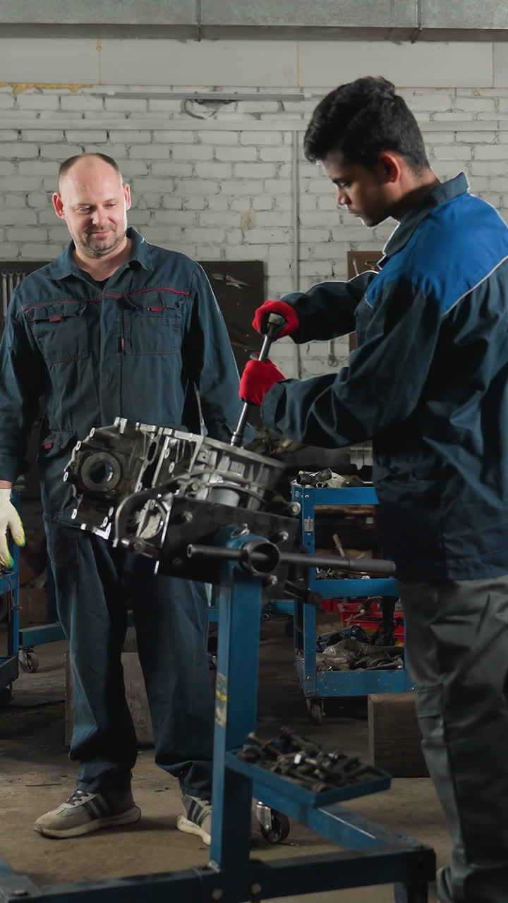 dos ingenieros mecánicos en un taller de automóviles, uno trabajando en un motor de coche mientras el colega observa, el fondo presenta coches estacionados, herramientas mecánicas y equipos de taller