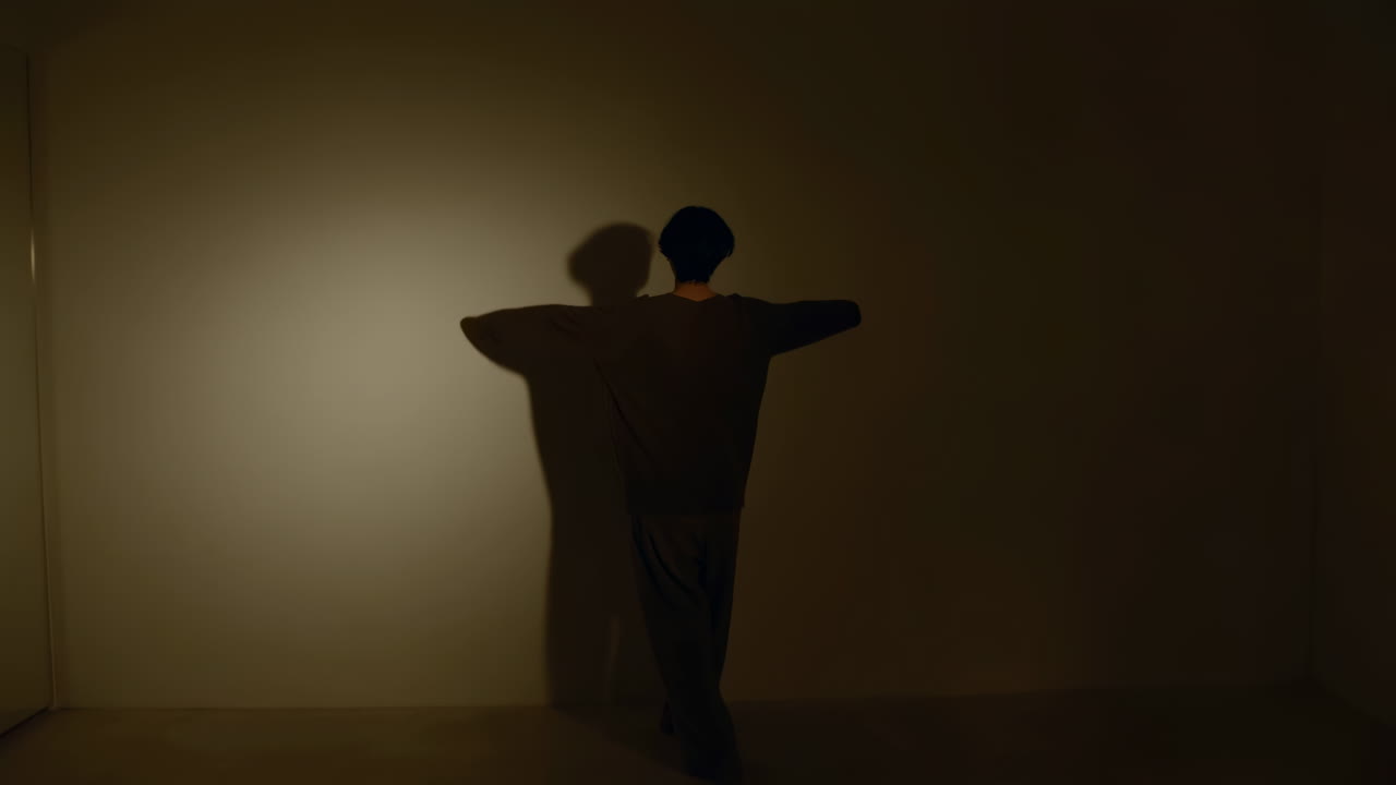 Solo Figure Facing Wall Silhouette, Slow Choreography And Shadow Play Under Warm Spotlight, Contemporary