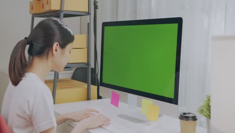 startup small business, young asian woman checking online order on computer with green screen. and packing boxes for products to send to customers.