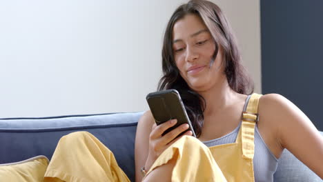 Happy-biracial-teenage-girl-sitting-on-couch-using-credit-card-and-smartphone-online,-slow-motion