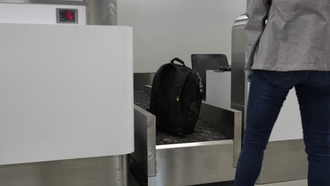 woman lifting her backpack at an airport security checkpoint with a digital weight display